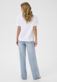 T-shirt en coton blanc avec une coupe décontractée, associé à un jean en denim bleu clair à jambes larges avec poches arrière et un délavage léger.
