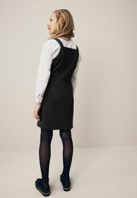 Zwarte wollen blend jurk met dikke bandjes, getailleerde taille en lengte boven de knie. Draag het over een wit long-sleeve shirt, gecombineerd met zwarte panty en schoenen.