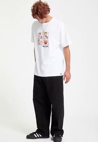 White short-sleeve t-shirt featuring colorful cartoon graphics and the brand name "Volcom" in the center, paired with black pants.