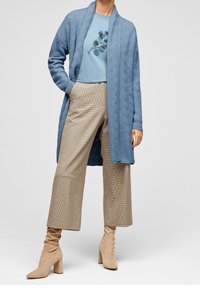 Cardigan lavorato a maglia azzurro chiaro sopra una t-shirt grafica azzurro chiaro, abbinato a pantaloni larghi a quadri beige e stivaletti con tacco beige.
