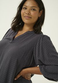 Blusa leggera di colore blu scuro con un motivo a pois testurizzati, scollatura a V e maniche a sbuffo, che presenta una vestibilità rilassata.