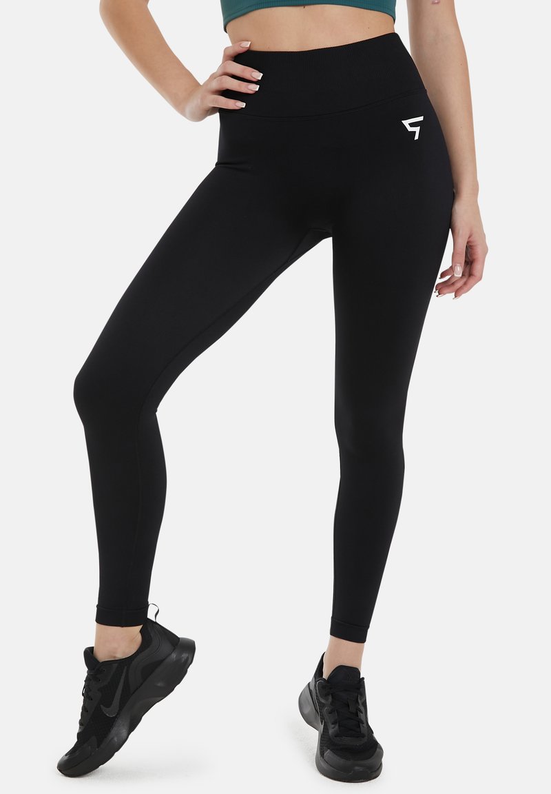 Črne visoko pasne legice iz raztegljive tkanine, z gladko teksturo in majhnim belim logotipom na stegnu.