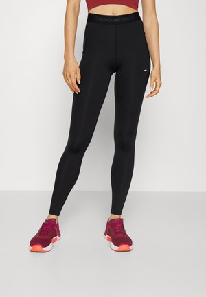 Leggings neri a vita alta con una texture liscia e logo Tommy Hilfiger in vita; abbinati a scarpe da ginnastica borgogna.