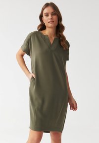 Olive green short-sleeve dress with a V-neckline, soft texture, and side pockets, featuring a straight cut and knee-length design.