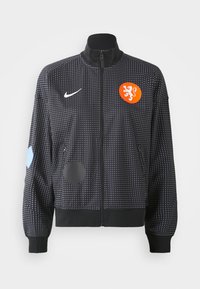 Černá zipová bunda s bílým tečkovaným vzorem, oranžovým lvím znakem a různými modrými a černými nášivkami na rukávech. Vyrobena z hladkého textilu.