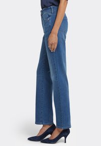 Blå denimjeans med vida ben och hög midja, med fickor fram och bak. Bärs med marinblå högklackade skor. Mjuk textur.