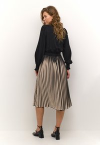 Svart långärmad topp i kombination med en beige kjol med svarta vertikala ränder, slät textur och klacksandaler.