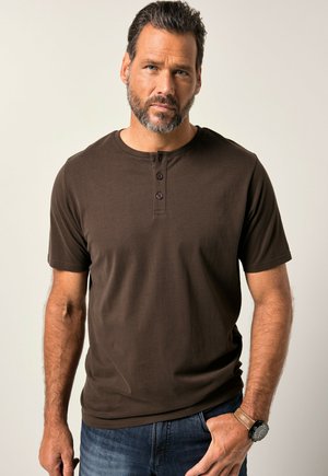 Camiseta Henley de manga corta marrón con cuello redondo y tapeta de tres botones. Textura suave, combinada con unos jeans de mezclilla azul y un reloj.