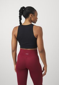Čierny rebrovaný crop top skombinovaný s vysokými bordovými legínami s logom na páske. Hladká textúra a priliehavý strih.