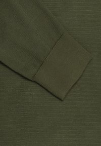 Tela de color verde oliva con una superficie texturizada y un puño acanalado en la manga, creando una apariencia limpia y estructurada.