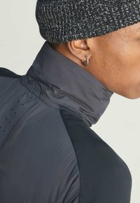 High-collared jacket featuring gray and black sections, made from a lightweight fabric with a smooth texture and perforated details on the back.