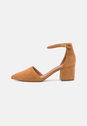 Escarpin fermé pour femme en daim beige avec bride à la cheville et talon moyen épais sur un fond clair uni.