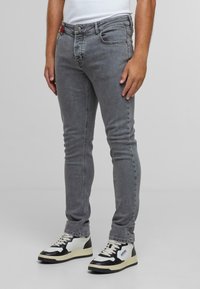 Jeans ajustados grises con una textura suave, cinco bolsillos y herrajes plateados. Combinados con zapatillas negras y blancas para un contraste.