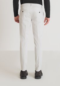 Pantaloni bianchi a gamba dritta con tasche posteriori, dettagli con bottoni e tessuto di cotone liscio. Indossati con scarpe scure, visti da dietro.