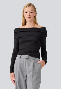 Top nero scollato sulle spalle con maniche lunghe, caratterizzato da dettagli arricciati sul colletto. Abbinato a pantaloni a vita alta in houndstooth grigio chiaro.