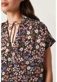 Bloemige blouse van lichtgewicht stof met een zwarte achtergrond, korte mouwen, V-hals en een strikdetail bij de kraag.