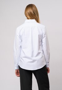 Heled sinine pika varrukaga nööbiga särk, millel on vertikaalsed triibud, klassikaline krae ja nööpidega mansetid. Kohandatud sobivus ja kaarjas hem.