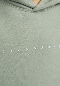 Sudadera verde clara de tejido suave con el nombre de la marca impreso "JACK & JONES" en letras blancas en el pecho.