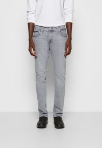 Vaqueros de mezclilla gris claro con corte ajustado, que presentan cinco bolsillos, detalles de costura sutiles y textura desgastada. Combinados con zapatillas negras.