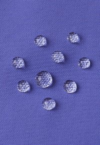 Des gouttes d'eau claires sur un fond de tissu texturé violet, de tailles variées, affichant une surface réfléchissante et des formes circulaires.