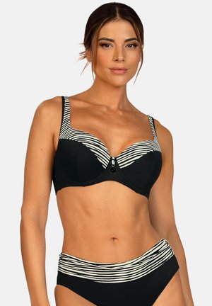 Kobieta ubrana w czarne bikini z białymi poziomymi paskami na górnej krawędzi i linii talii, pozująca na jasnym, jednolitym tle.