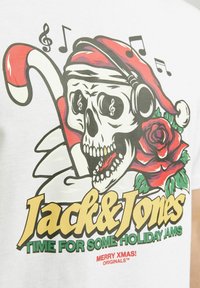 Bílá tričko s grafickým motivem lebky v santovské čepici, s cukrovou holí, růžemi a hudebními notami. Text zní "Jack & Jones."