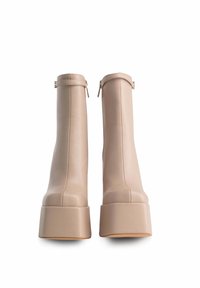 Stivaletti beige in pelle con suola piatta chunky e chiusura con zip sul retro, caratterizzati da una texture liscia e un design strutturato.