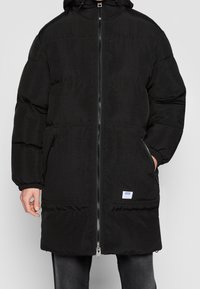 Sort dunjakke med lynlåsføring foran, hætte og to sidelommer. Fremstillet af glat, tekstureret stof med en afslappet pasform.