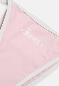 Ροζ ύφασμα με λευκή επένδυση που φέρει τη λέξη "Juicy" σε λευκή γοτθική γραμματοσειρά και δύο μικρές καρδιές, πιθανό να αποτελεί μέρος ρούχου.