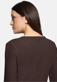 Braunes, strukturiertes Langarm-Oberteil mit Rundhalsausschnitt. Verfügt über dezente Rippenstruktur und eine lockere Passform, die den hinteren Halsausschnitt und die Schulterdetails hervorhebt.
