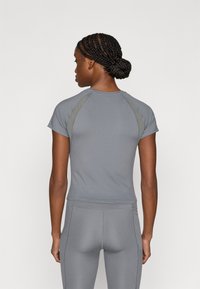 Sivi sportski top s kratkim rukavima, s raglan šavovima i prilagođenim krojem. Glatka tekstura i minimalistički stil.