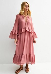 Lång rosafärgad klänning med volangärmar och volangkant, med nyckelhålsknäppning och dragsko, tillverkad av lättviktsmaterial.