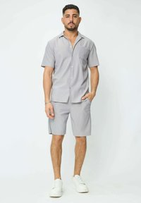 Chemise à manches courtes gris clair avec une poche et un short assorti, présentant de fines rayures verticales. Porté avec des baskets blanches.