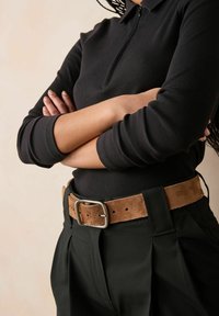 Mustmustriibuline lukuga ülemine, mis on kombineeritud volditud mustade pükstega ja pruunist nahast vööga, millel on ristkülikukujuline metallist klamber.