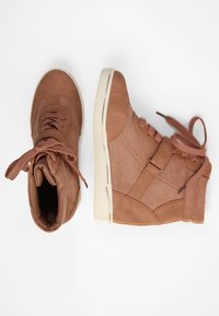 Pár hnědých vysokých tenisek s tkaničkami a páskem, pohled shora a ze strany na bílém pozadí.