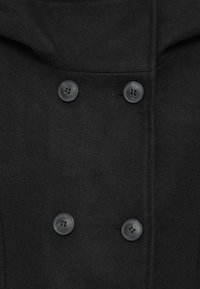 Black double-breasted coat front with four large round black buttons in two vertical rows on wool fabric.