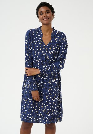 Langsleeve blauwe jurk met een V-hals, voorzien van een verspreid stippenpatroon in wit, goud en zwart; zachte, vloeiende stof.