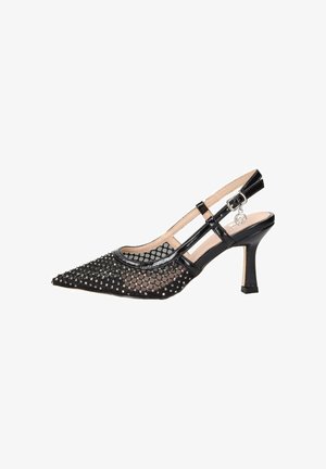 Scarpa con tacco alto a punta in rete nera con decorazioni di cristalli, cinturino alla caviglia con fibbia e charm decorativo su sfondo bianco.