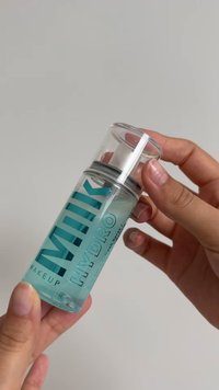 Transparante sprayfles met een pompje, gevuld met een blauwe vloeistof, opvallende witte en turquoise tekst, en een doorzichtige dop. Hand die de fles vasthoudt.