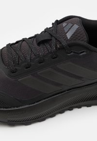 Black athletic shoe with mesh fabric upper, rubber sole, textured detailing, and three diagonal stripes. Features reinforced toe and lacing system.