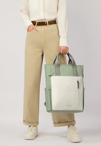 Borsa tote spaziosa in verde chiaro e bianco, con texture liscia, doppio manico grigio e tasca frontale con zip e dettaglio del logo.