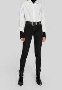 Black skinny jeans with a high waist, paired with a white button-up shirt and a thick black belt featuring a silver buckle. Black ankle boots.