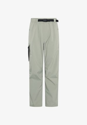 Beiges Baumwoll-T-Shirt mit fischemotiviertem schwarzem Druck. Hellgrüne Nylonhose, legerer Schnitt, mit Seitentaschen und schwarzen Akzenten. Weiße Sneakers.