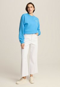 Jasnoniebieski sweter z długimi rękawami i okrągłym dekoltem, w połączeniu z białymi spodniami o szerokich nogawkach z wysokim stanem i kremowymi sneakersami.