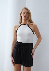 Top halter blanco con ribete negro, combinado con pantalones cortos negros de talle alto con una cinturilla con volantes y detalle de cinturón atado.
