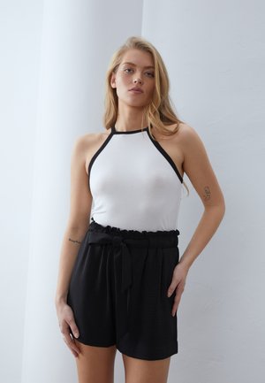 Top halter blanco con ribete negro, combinado con pantalones cortos negros de talle alto con una cinturilla con volantes y detalle de cinturón atado.