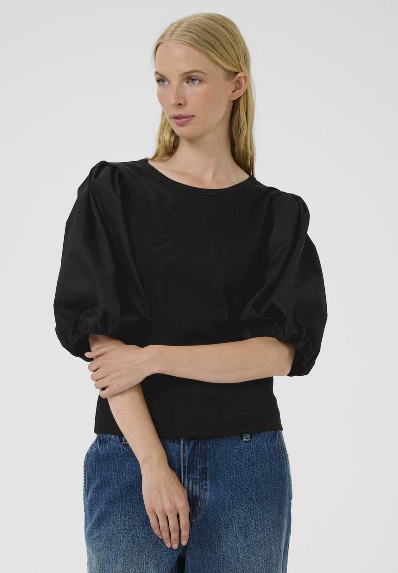 Musthave mustribiid materjalist must puff-sleeve topp, ümmarguse kaelusega ja kinnise taljega, koos siniste teksadega.