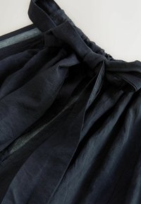 Sötét szövetből készült szoknya nagy, megkötött masnival az összegyűrt derékrészen, kiemelve a textúrát és a redőket.