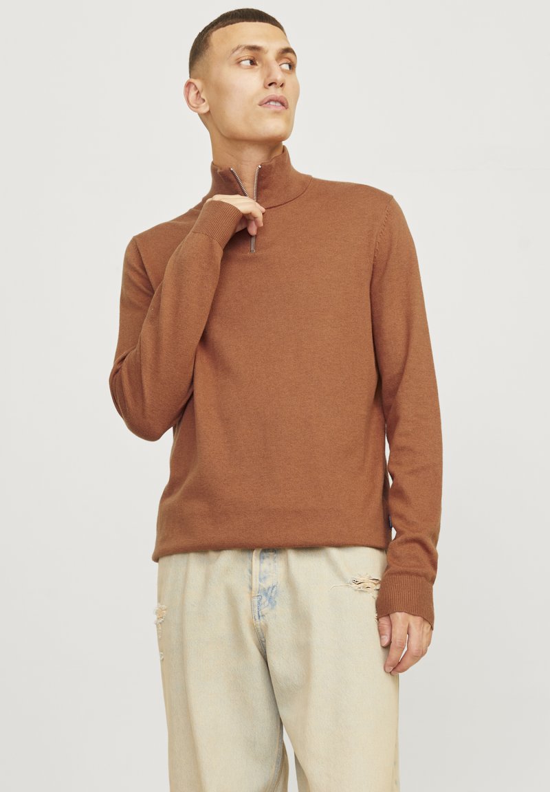 Bruine sweater met rits en een slanke pasvorm, geribbelde manchetten en een zachte textuur, gecombineerd met licht verwoeste spijkerbroek.