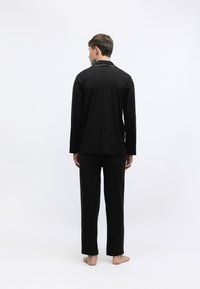 El conjunto de salón negro presenta una blusa de manga larga y pantalones holgados, fabricados con un material suave de textura lisa y un diseño minimalista.